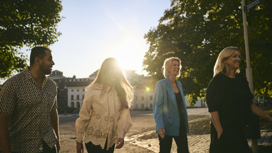 Glada kollegor promenerar skrattande tillsammans utomhus en solig sommarkväll.