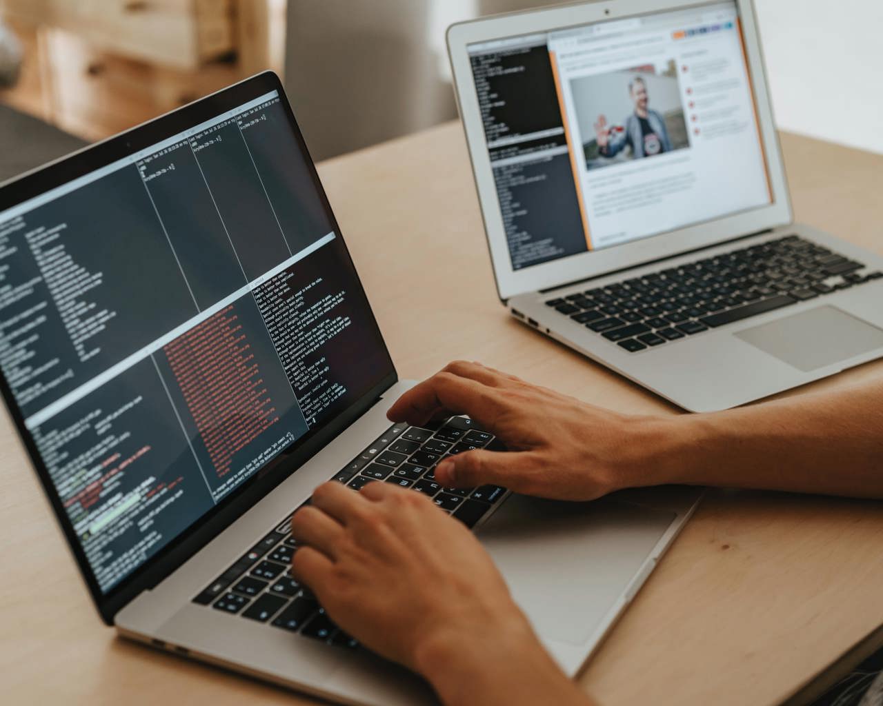 Två laptops står på ett bord, en person programmerar på den ena datorn.