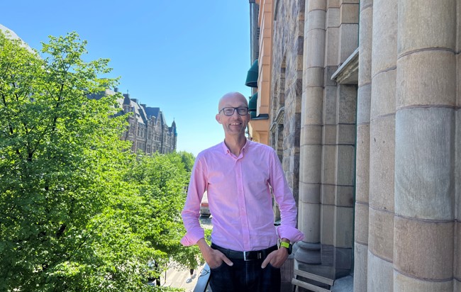 Per Norstad, iklädd en rosa skjorta, står på en balkong på Zingtons kontor och njuter av en solig dag med klarblå himmel.