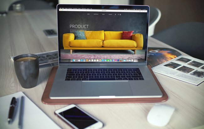 Mac-dator står på ett skrivbord och visar en e-handelssida med en soffa.