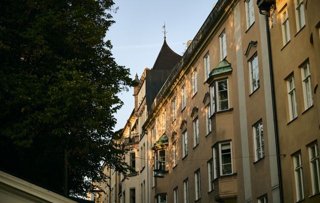 Byggnad badande i varm sensommarsol, omgiven av lummiga träd.